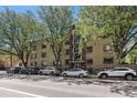 An exterior view of a multi-unit residential building on a tree-lined street with many parked cars at 500 E 11Th Ave # 102, Denver, CO 80203