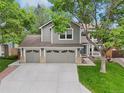 Two-story gray home featuring a three-car garage, landscaped yard, and mature tree at 6726 W 97Th Cir, Westminster, CO 80021