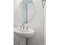 Elegant pedestal sink with oval mirror and modern fixtures in a bright, minimalist bathroom at 9277 Truckee Ct, Commerce City, CO 80022