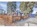 View of a charming blue home with a wood fence, gravel driveway, and mature trees at 5725 W Mississippi Ave, Lakewood, CO 80226