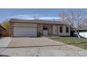 Inviting single-story home with a spacious driveway, an attached garage, and a front yard with mature tree at 265 Cleveland Ct, Bennett, CO 80102