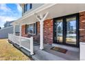 Inviting front porch featuring a seating area, brick accents, and black framed glass front doors at 7631 Oak St, Arvada, CO 80005