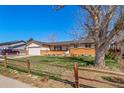 Front exterior featuring a well maintained home, lawn, mature trees, and a classic wooden fence at 9231 W Louisiana Ave, Lakewood, CO 80232