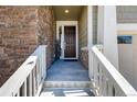 Covered front entryway with brick wall detail, concrete stairs and wooden door leading into the home at 8230 S White Crow St, Aurora, CO 80016