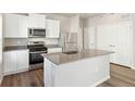 Well-lit kitchen boasts stainless steel appliances, white cabinets, a center island, and wood-look flooring at 2986 Oxley St, Strasburg, CO 80136
