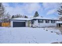 Charming single-story home with a dark gray garage door and snow-covered front yard and a yellow front door at 3091 S Krameria St, Denver, CO 80222