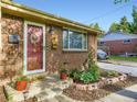 Close-up of a red front door adorned with a wreath, surrounded by flower pots and a well-maintained garden bed at 6664 Gray St, Arvada, CO 80003