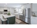 Bright kitchen featuring white cabinetry, stainless steel appliances, quartz counters, and a green island with seating at 6526 S Cherry Way, Centennial, CO 80121