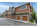 Townhome garages with brown doors, complemented by stone accents and well-manicured landscaping at 7130 Simms St # 206, Arvada, CO 80004
