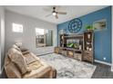 Living room featuring a blue accent wall, ceiling fan, rustic entertainment center, and a large window at 6777 Larsh Dr, Denver, CO 80221