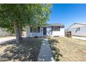 Inviting single-story home with gray siding, black door, and well-maintained front yard under a clear blue sky at 7111 Clermont St, Commerce City, CO 80022