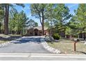 Charming ranch-style home nestled among mature pine trees with a long driveway and stone accents at 670 Independence Dr, Larkspur, CO 80118