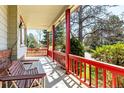 Cozy front porch with red railings and supports, benches, and a view of the lush, landscaped yard at 2912 Lake Park Way, Longmont, CO 80503