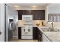 Modern kitchen with stainless steel appliances, granite countertops, and dark wood cabinets at 5506 S Quemoy Cir, Aurora, CO 80015