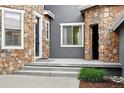 Inviting front porch area featuring stone accents, a modern black door, and gray concrete steps at 2832 Danbury Ave, Highlands Ranch, CO 80126
