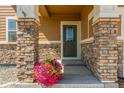 Close up of the front door, showing the stone facade and inviting front porch decor with beautiful flowers at 1933 Griffin Dr, Brighton, CO 80601