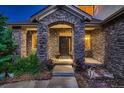 Stone facade entryway with double doors, lighted at night, and lush landscaping at 5458 W Calhoun Ave, Littleton, CO 80123