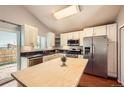 Bright kitchen features stainless steel appliances, light wood island and white cabinetry at 5587 S Simms Way, Littleton, CO 80127