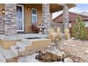 Inviting front porch featuring stone columns, decorative welcome sign, and a tranquil rock water feature at 6731 Pinery Villa Pl, Parker, CO 80134