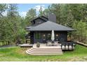 Beautiful exterior of a home showing the deck with outdoor seating with views of mature trees and a manicured lawn at 28833 Western Dr, Evergreen, CO 80439