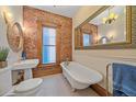 Bright bathroom with clawfoot tub, exposed brick wall, pedestal sink, and decorative mirror for vintage charm at 1356 N Marion St, Denver, CO 80218
