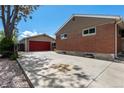 View of the brick house and detached garage with a red door and concrete driveway on a sunny day at 160 Northglenn Dr, Northglenn, CO 80233