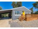 Gray single-story home boasting a wooden porch, bright yellow front door, and carport at 695 S Quitman St, Denver, CO 80219