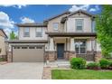 Charming two-story home featuring a manicured lawn and a welcoming front porch with stone accents at 676 Fossil Bed Cir, Erie, CO 80516