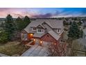 Attractive home showcases red brick, neutral siding, mature trees, and a two-car garage at dusk at 7086 Esperanza Dr, Castle Pines, CO 80108