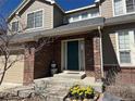 Close-up of a home's front entrance with a teal door, brick facade, and blossoming yellow flowers at 5520 Morgan Way, Frederick, CO 80504