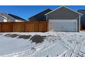 Two-car garage with attached house, wooden fence in snowy yard at 2981 Pershing Street, Strasburg, CO 80136