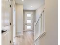 Bright hallway featuring light wood floors, a white front door with decorative windows, and a staircase at 9629 Browns Peak Cir, Littleton, CO 80125
