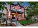 Charming two-story pink home with a lovely wrought iron fenced yard and flowering planters on porch at 2721 Curtis St, Denver, CO 80205