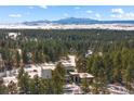 Breathtaking aerial view of a modern home surrounded by a lush forest, with snow-capped mountains in the distance at 367 Sandy Hollow Trl, Franktown, CO 80116