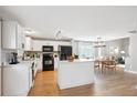 Eat-in kitchen boasts white cabinets, an island, black appliances, and wood flooring, flowing into dining at 14625 Vine St, Thornton, CO 80602