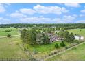 Beautiful fenced property with a home, barn, and green pasture land with a backdrop of mature trees under a partly cloudy sky at 497 Grey Squirrel Way, Franktown, CO 80116