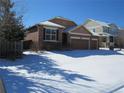 View of the home's exterior with brick facade and a two-car garage, surrounded by a snowy landscape at 25858 E Bayaud Ave, Aurora, CO 80018