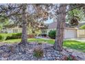 Landscaped front yard featuring mature trees, rocks, and plants enhancing the curb appeal of the home at 6055 W Warren, Lakewood, CO 80227