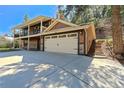 Exterior elevation of a home showcasing a two car garage with beautiful landscaping and a stone staircase at 7134 Kiowa Rd, Larkspur, CO 80118