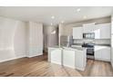 Bright kitchen boasts stainless appliances, white cabinets, central island and hardwood floors at 2974 Oxley St, Strasburg, CO 80136