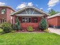 Charming brick home featuring a well-manicured lawn, garden beds, and covered porch at 660 S Clarkson St, Denver, CO 80209