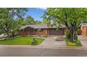 Charming brick ranch-style home with mature trees, lush green lawn, and an attached two-car garage at 7077 Dudley Dr, Arvada, CO 80004