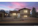 Two-story home with neutral siding, brown roof, gravel yard, chain-link fence, and colorful sky at 7611 Fernando Rd, Denver, CO 80221