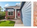 Inviting front entrance featuring a well-kept garden, brick accents, and a pop of color from the red door at 7061 Palisade Dr, Highlands Ranch, CO 80130