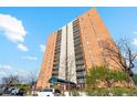 A tall brick apartment building stands under a blue sky with minimal landscaping around the entrance at 955 Eudora St # 801E, Denver, CO 80220
