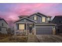 Charming two-story home featuring a welcoming front porch, grey siding and an attached two-car garage at dusk at 5657 Jaguar Way, Lone Tree, CO 80124