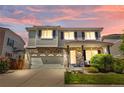 Charming two-story home featuring a brick facade, well-maintained lawn, and attached two-car garage at dusk at 15353 E 98Th Pl, Commerce City, CO 80022