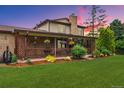 View of the covered patio, brick chimney, landscaped yard, complete with beautiful flowers and a lush lawn at 5954 W Leawood Dr, Littleton, CO 80123