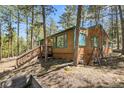 Cozy wood cabin exterior featuring green trim, surrounded by tall pine trees, and hillside landscape at 5235 Cheyenne Rd, Indian Hills, CO 80454