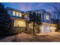 Charming two-story home at dusk with stone accents, covered porch and attached three-car garage at 683 Ridgemont Cir, Highlands Ranch, CO 80126